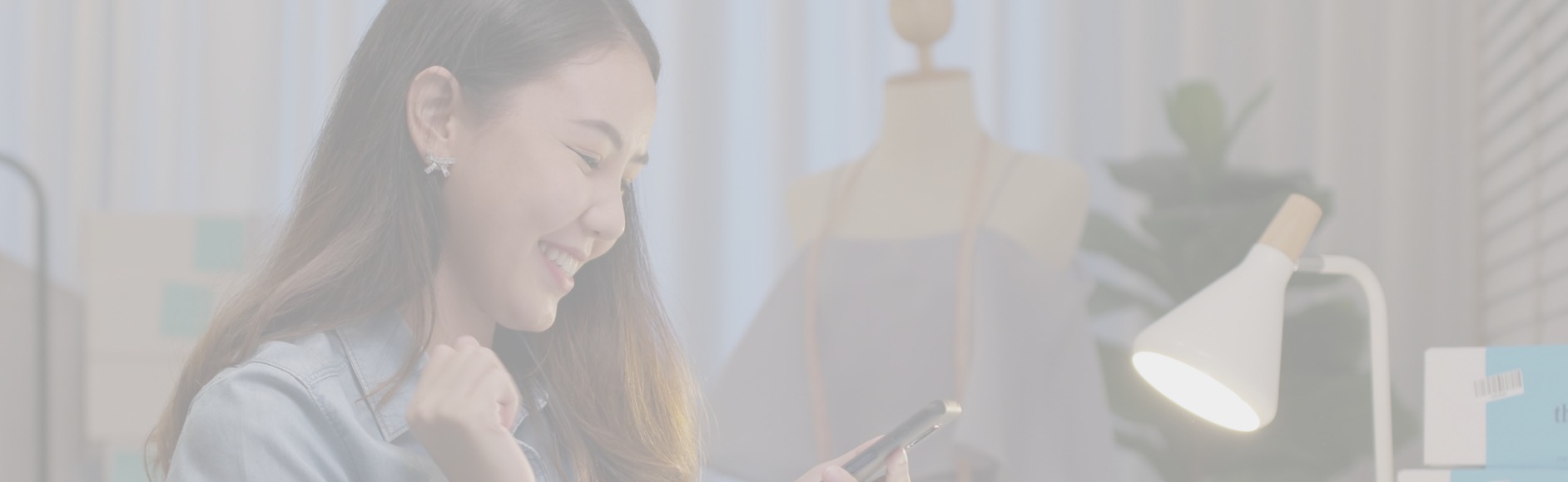 magenta colored image of student smiling at desk while holding phone